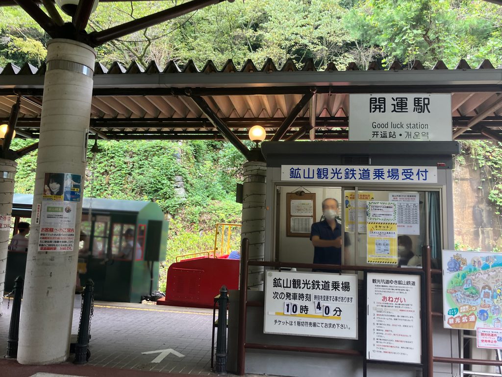 「開運駅」の乗り場、次の発車時刻「10時40分」の掲示板とトロッコ車両