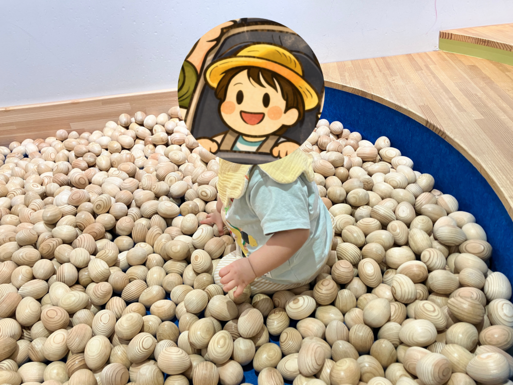 卵形の木製ボールが敷き詰められたボールプールで遊ぶ赤ちゃん